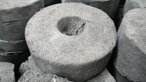 Close-up of several cylindrical briquettes made of compressed magnesium. Each briquette has a uniform, rough texture with a central hole running through it, typical of fuel briquettes used for burning. The surface is slightly fibrous.