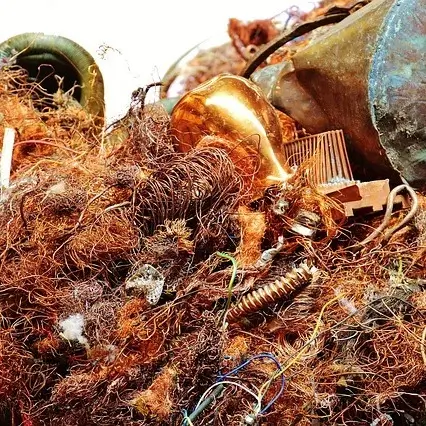 Tangled heap of various metal scraps, including copper wires, springs, and other disassembled components. The wires are frayed and twisted, creating a chaotic, dense mass of reddish-brown material. Among the wires, there are also pieces of brass, from old fixtures or instruments, adding a golden shine to the mix.