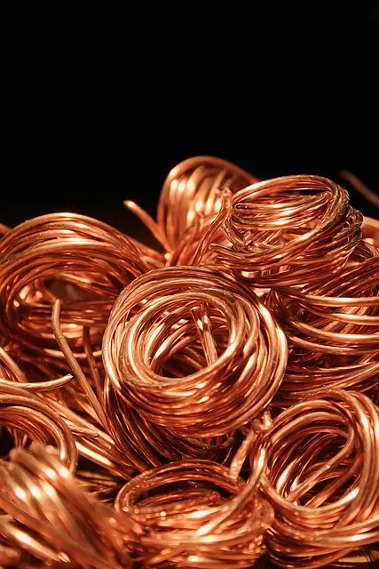 Close-up of several coiled copper wires, neatly arranged in tight loops. The copper has a bright, shiny appearance, with its characteristic reddish-brown hue, reflecting light and giving the wires a lustrous, metallic sheen. The coils are stacked together, creating a visually appealing pattern of intertwined loops.