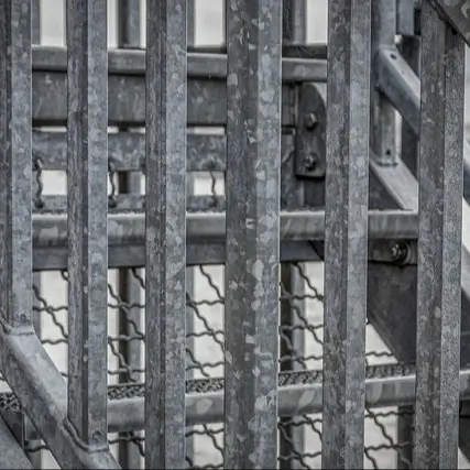 Close-up view of zinc-made structure, with a weathered, industrial appearance. The vertical and horizontal bars create a grid-like pattern, with some parts showing signs of wear and rust spots. The bars are thick and sturdy.