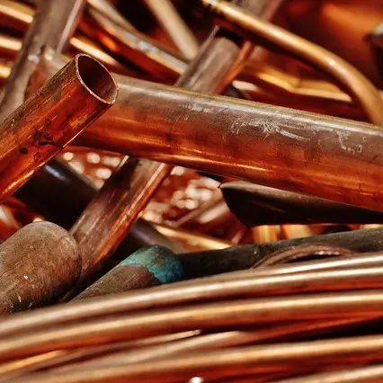 Pile of shiny copper pipes and tubing, some straight and others bent. The copper has a rich, reddish-brown color, with a few areas showing slight tarnishing. The pipes vary in diameter and length, and their smooth, reflective surfaces catch the light.