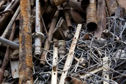 The image shows a pile of rusty, discarded lead objects, including pipes, rods, and twisted wires. The metal pieces are corroded and weathered, with varying shades of brown and orange rust. The pipes and rods are jumbled together, some with open ends, and the wires are tangled, creating a chaotic, cluttered appearance.