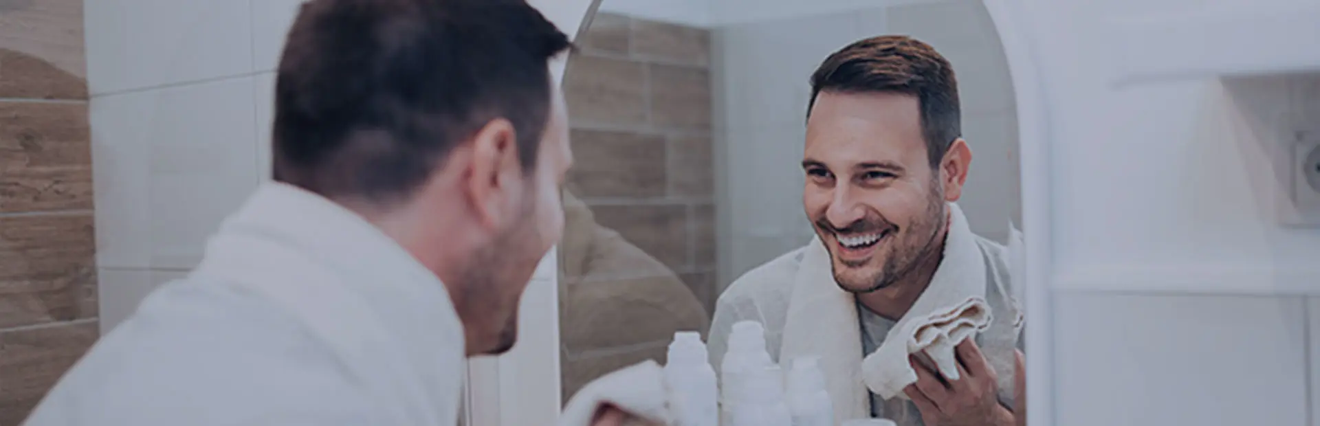 A man in his 40s sits in front of a white laptop, smiling as he learns about how to clean partial dentures on the Fixodent website.