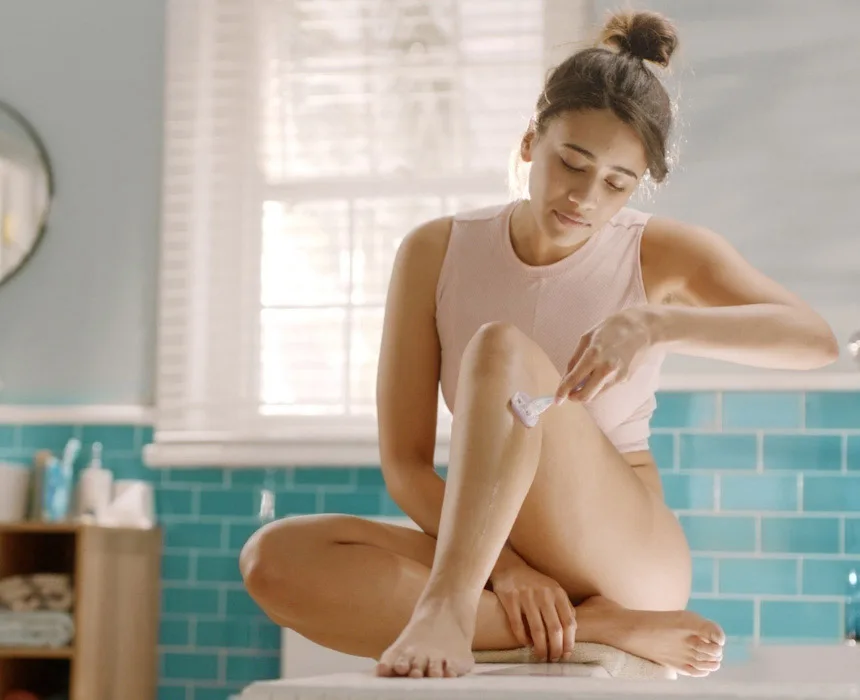 Mujer afeitándose la pierna mientras está sentada en el baño