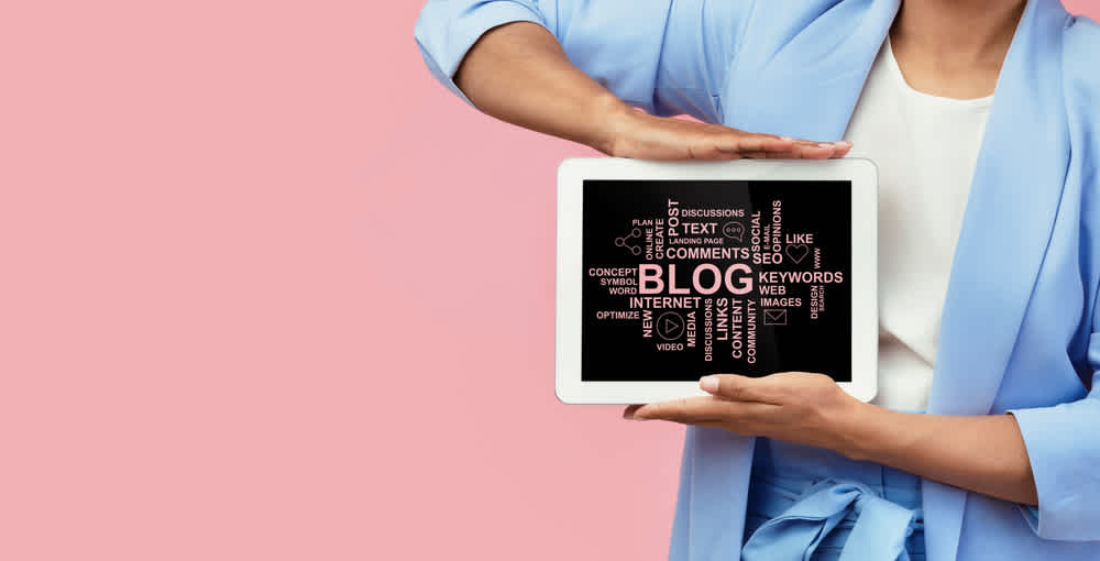 Female hands showing tablet computer with essential blogging terms on screen against pink background