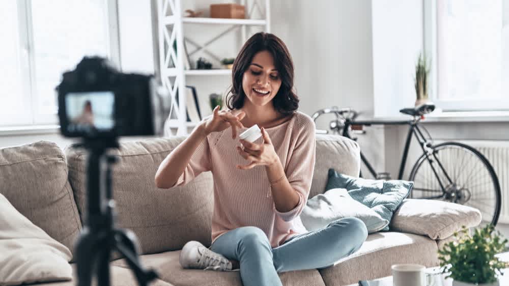 Young woman testing beauty product and smiling while making social media video - How to Make Product Videos for Shopify to Increase Sales - Clipchamp blog