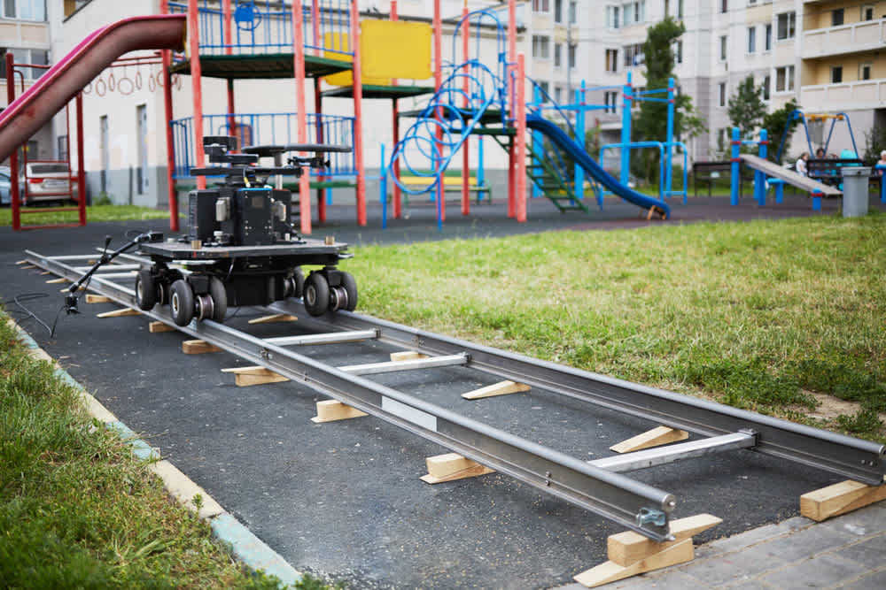 Cameraman dolly stands on rails mounted at children playground in courtyard