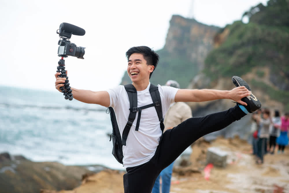 Travel vlogger holds his camera on a tripod and smiles