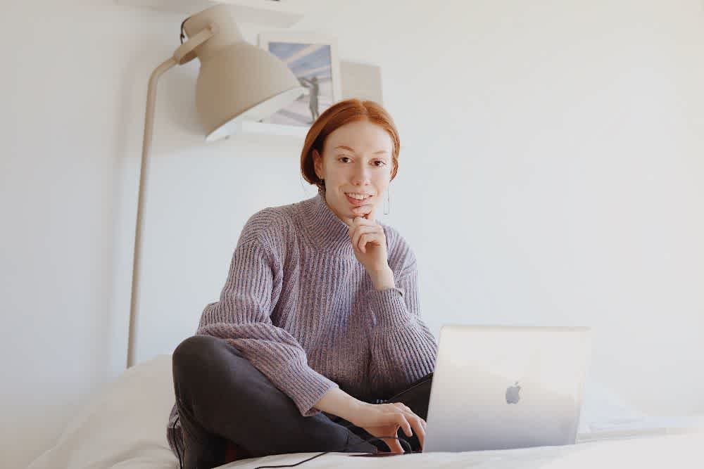 A young woman smiles while working on her laptop