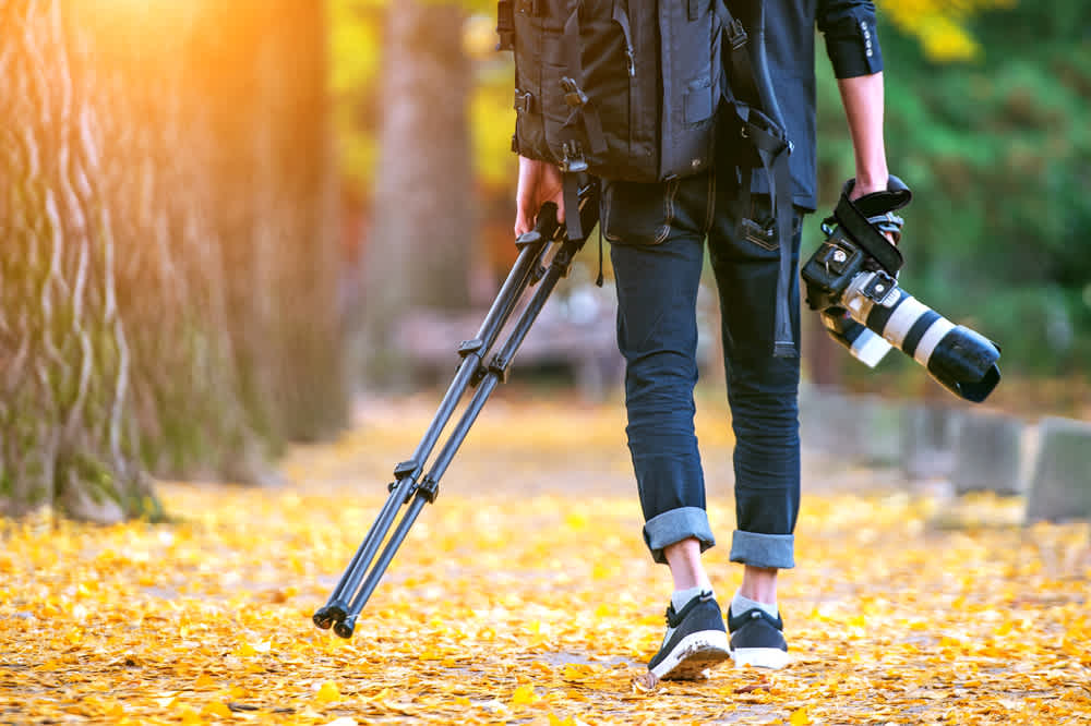 professional photographer with camera and tripod in autumn- 5 Essentials You Need In Your Video Camera Bag For A Day Shoot - Clipchamp Blog