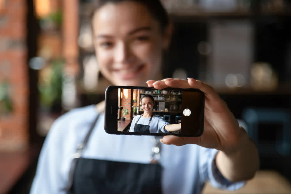 happy smiling female business owner in apron taking selfie video - How to make a promo video - Clipchamp blog
