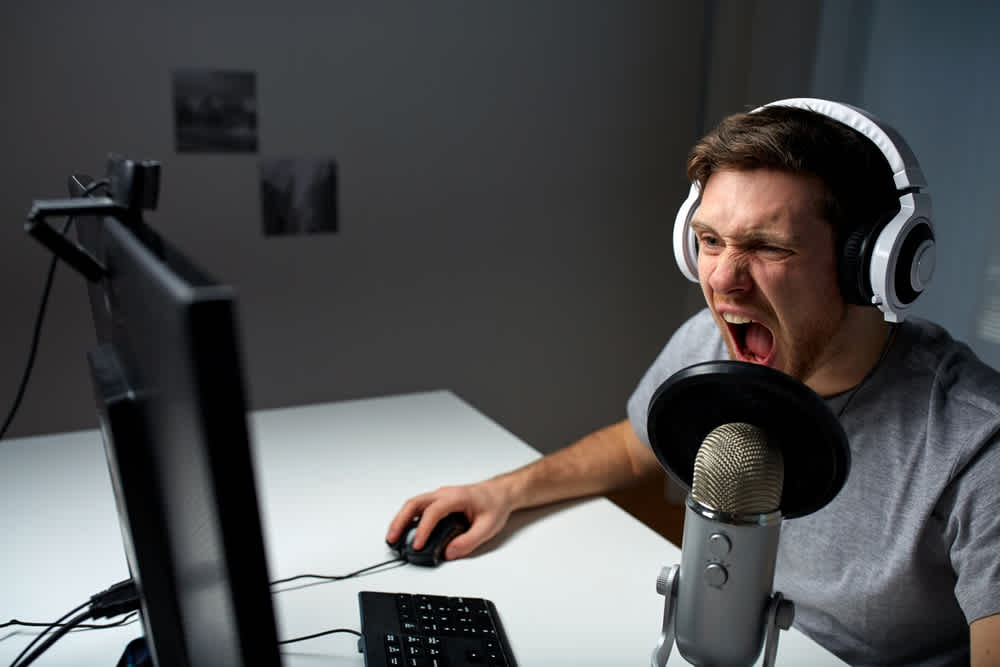 Gaming YouTuber wearing a headset connected to a microphone and livestreaming his computer gameplay