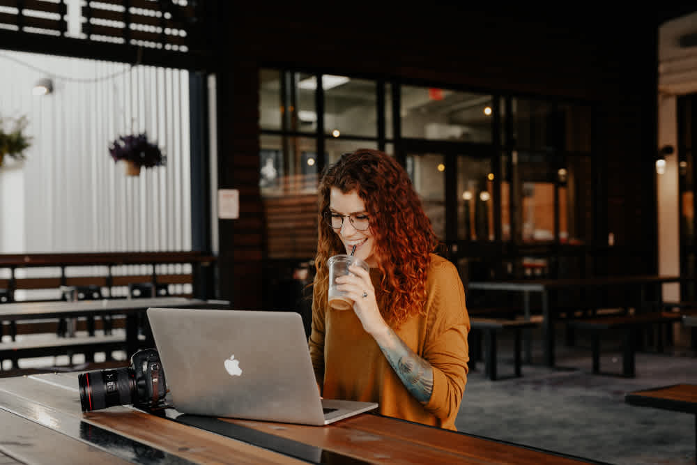 A woman works at her laptop while sipping an iced coffee.
