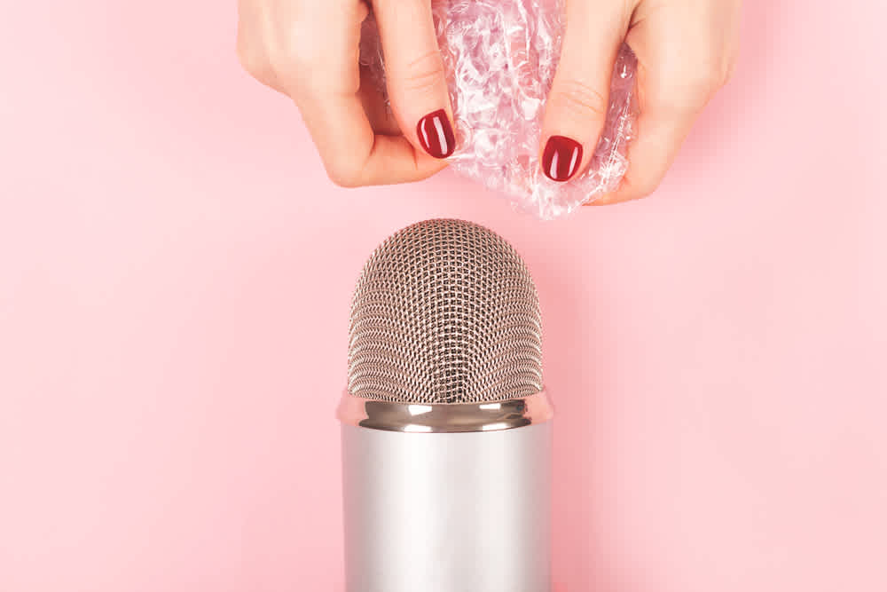 ASMR YouTuber creating sound effects near a microphone with saran wrap