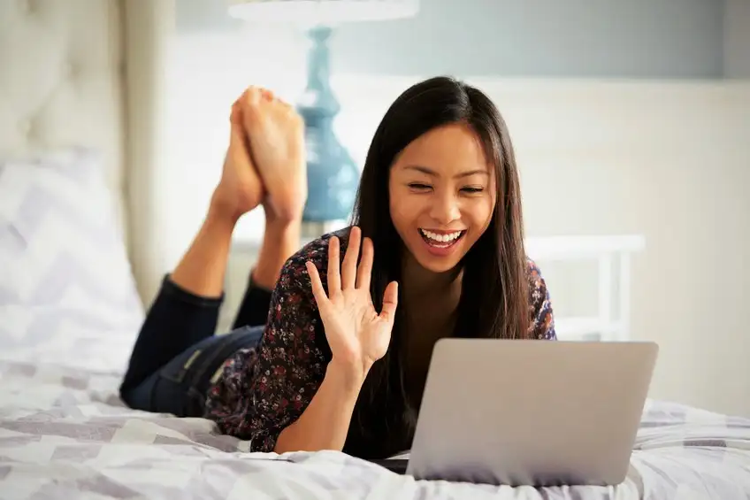 Woman Relaxing On Bed Using Laptop Computer For Video Call