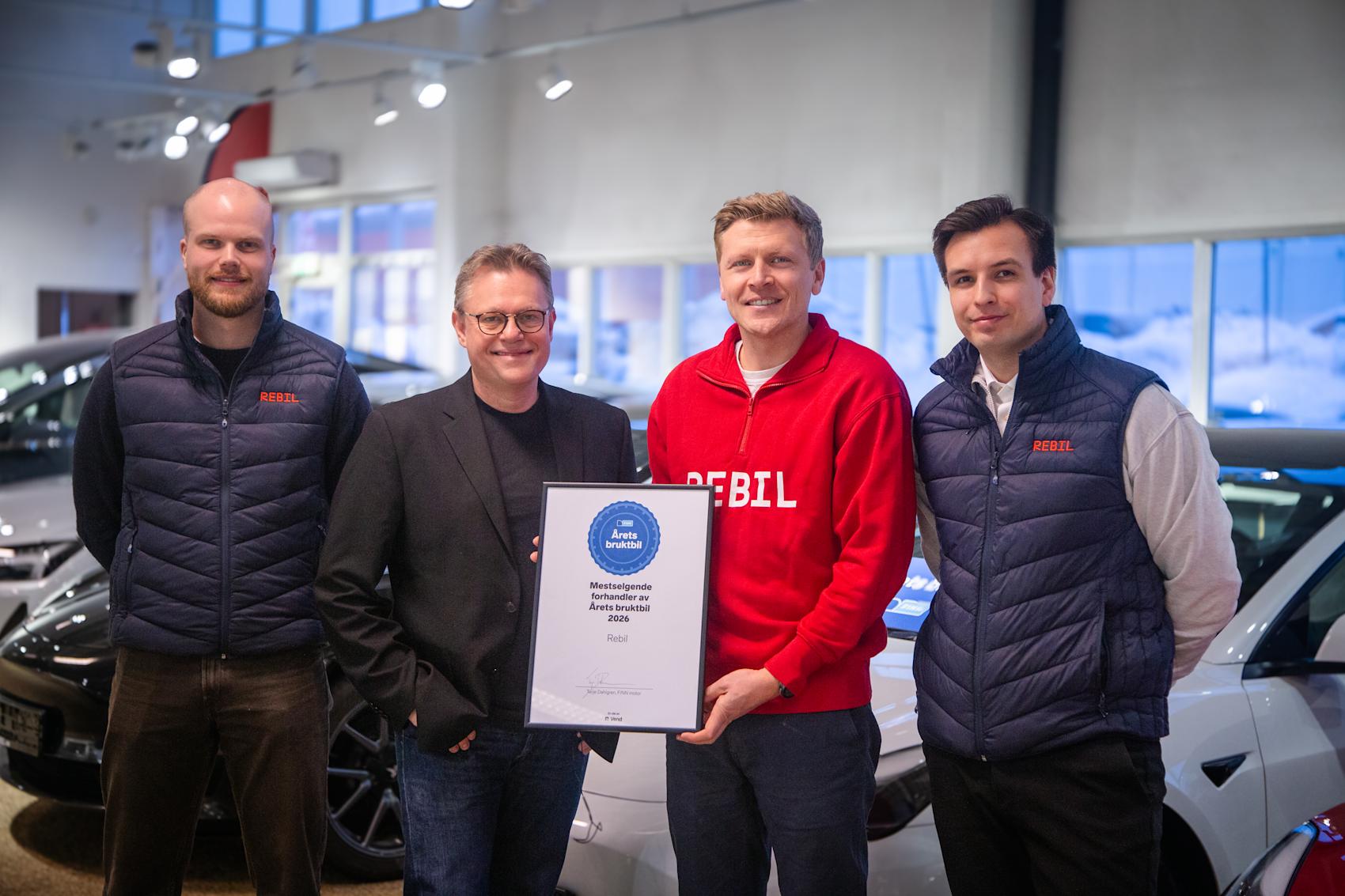 Fire personer i en bilforretning holder et diplom for "Årets bruktbil 2024". Rebil-logo synlig på klær og diplom.