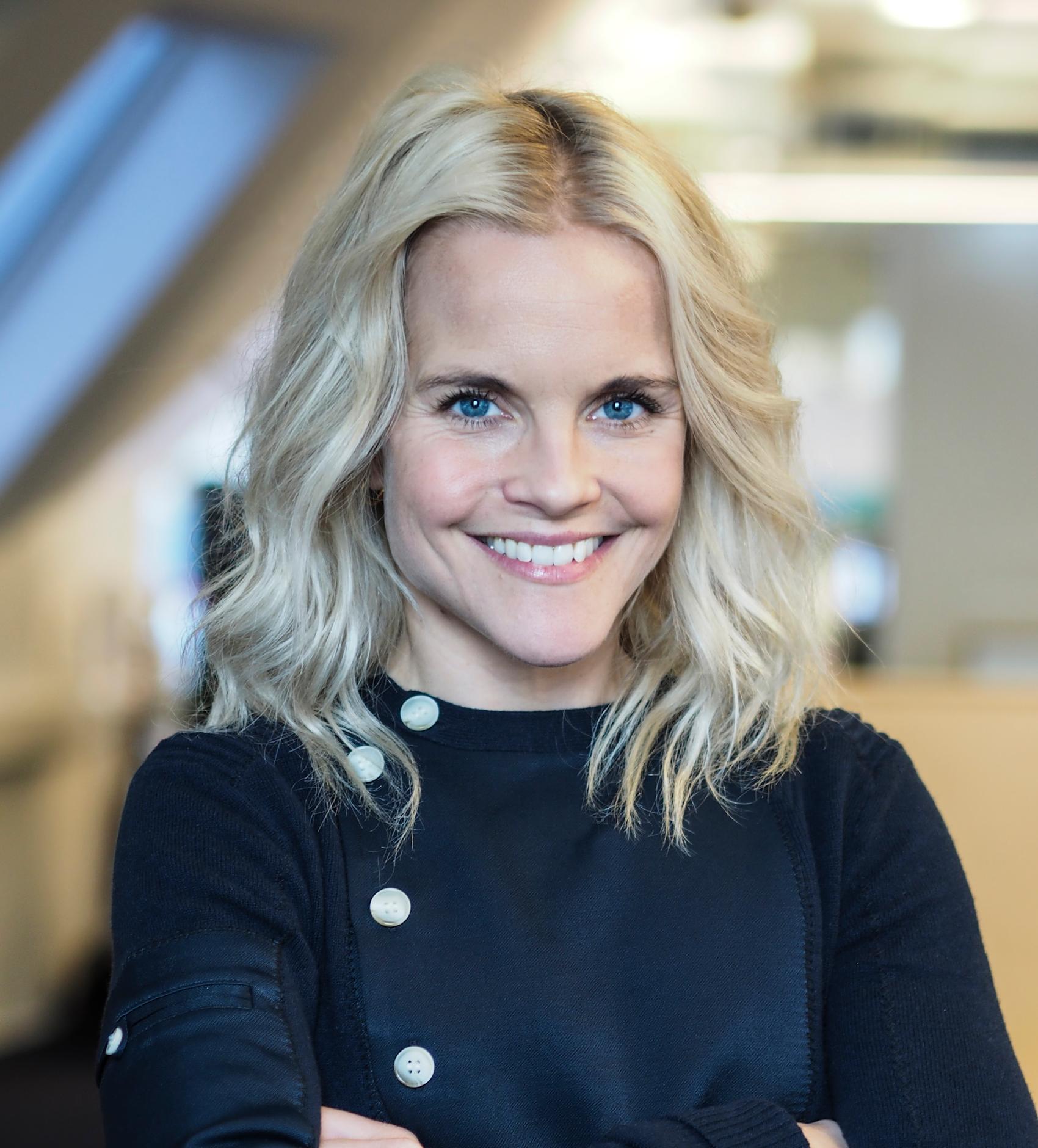 Et portrett av kommunikasjonssjef i FINN, Adele Cappelen Blystad. Hun har blondt skulderlangt hår og smiler bredt mot kameraet, ikledd en blå cardigan med hvite knapper.