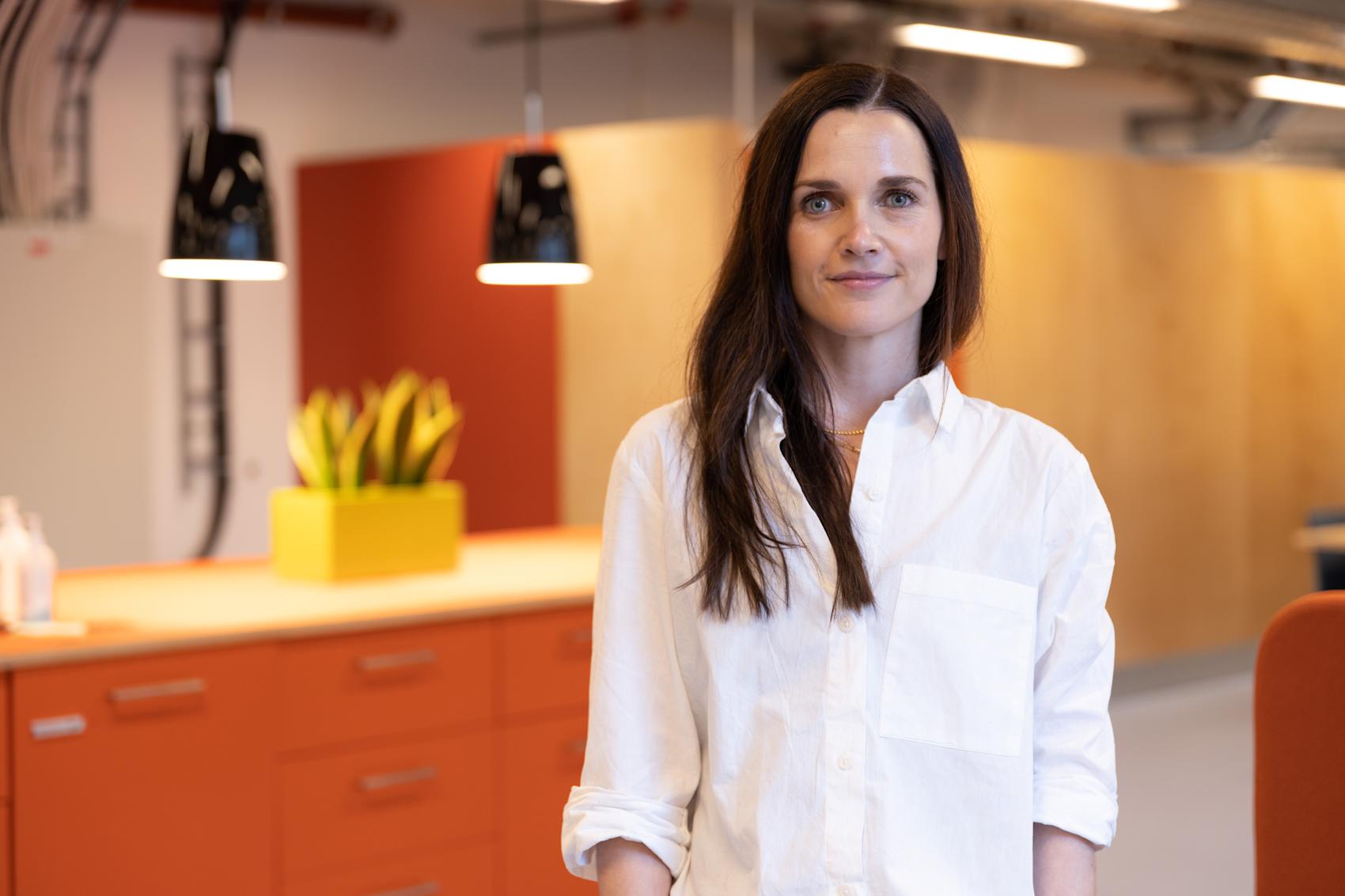 Bildet viser Hanne Revholt, seniorrådgiver innen HR i Skatteetaten. Hun har brunt, løst hår, smiler mot kameraet, og er kledd i en hvit skjorte.