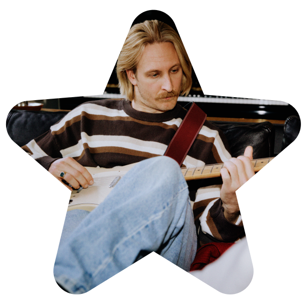 En mann med blondt hår og bart spiller elektrisk gitar. Han har stripete genser og jeans, og bildet er formet som en stjerne.
