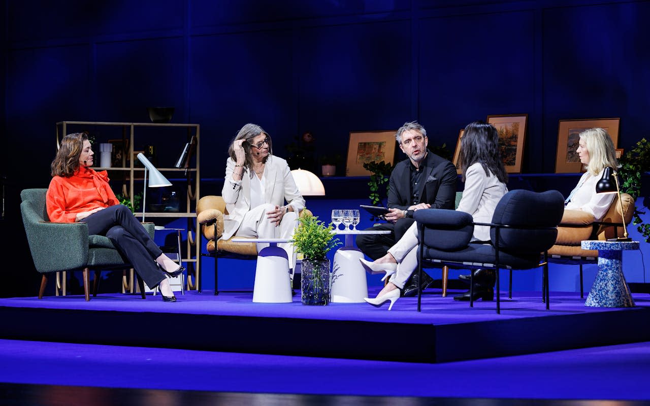 Fem personer på scenen sitter i stoler under en paneldebatt