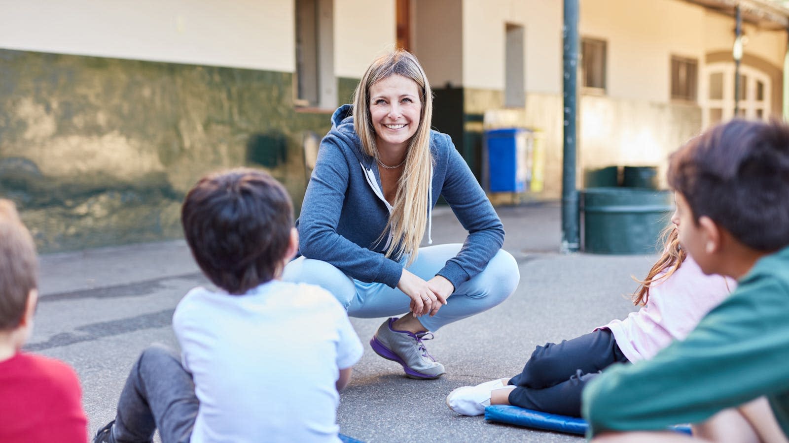 En kvinnelig lærer sitter på huk foran skolebarn