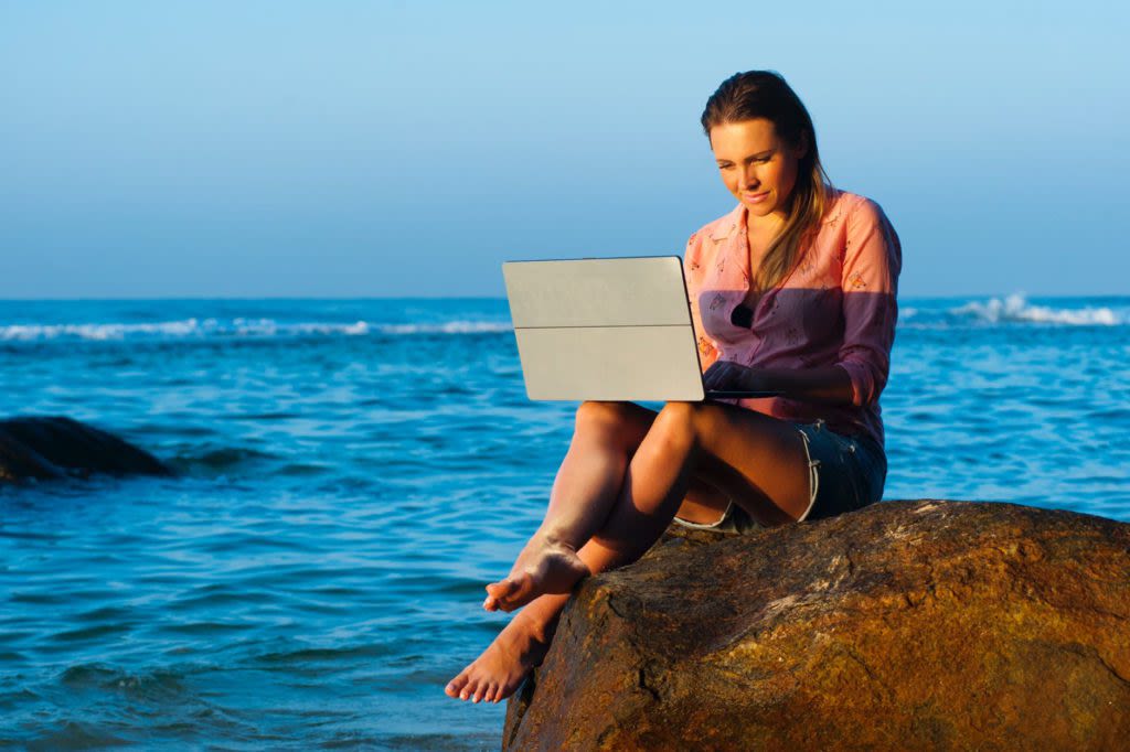 Mujer nómada digital trabajando en la playa