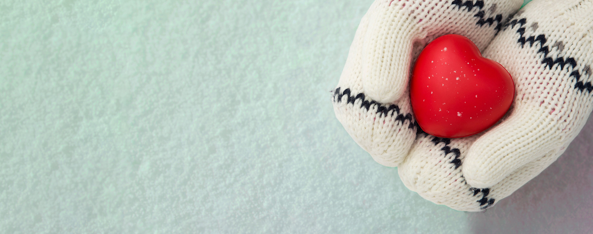 In the snow, warm mittens hold a red heart with care.