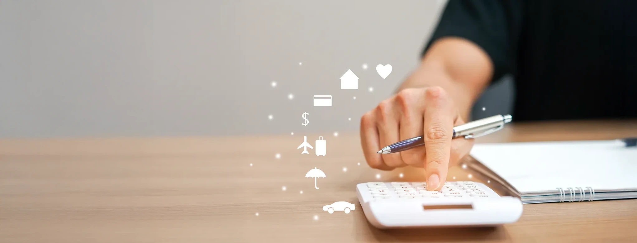 Une main appuie sur les touches d'une calculatrice tout en tenant un stylo. Un cahier est posé à côté de la calculatrice et des icônes blanches flottent autour de la main : un cœur, une maison, une carte de crédit, le symbole du dollar, un avion et une valise, un parapluie et une voiture.