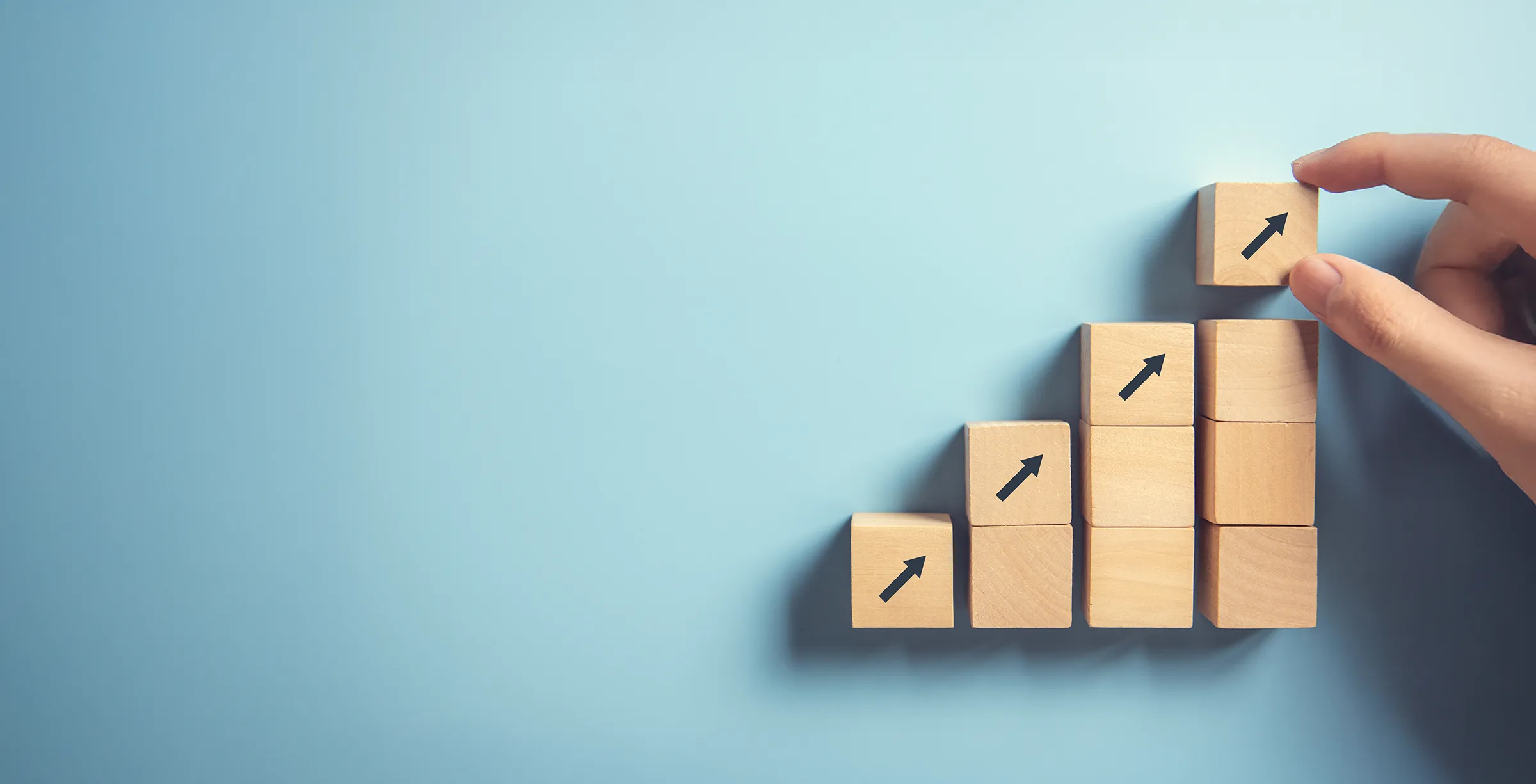 A hand arranges wooden blocks in rows. Together, they form a staircase-like chart with a few blocks with arrows pointing upward.