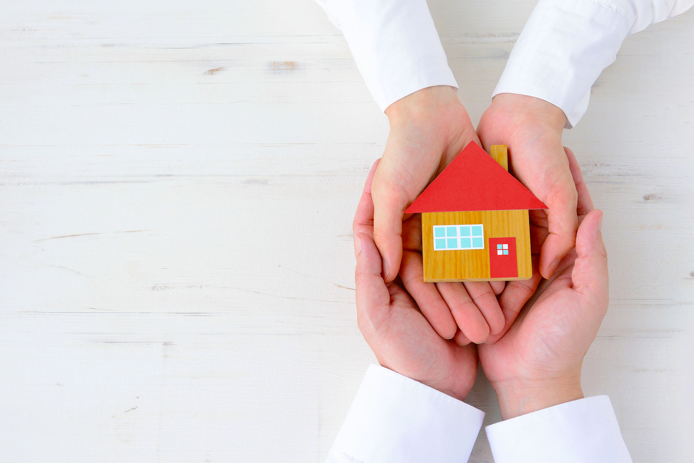 Les mains d’un parent tiennent les mains d’un enfant, alors que celui-ci tient une maisonette de bois.