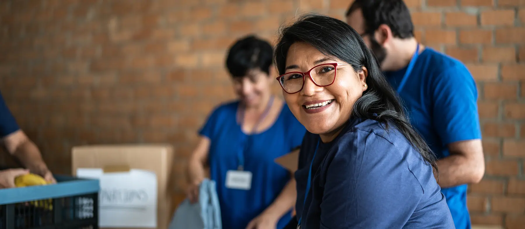 While volunteering with a group of people, a woman looks straight at the camera and smiles.