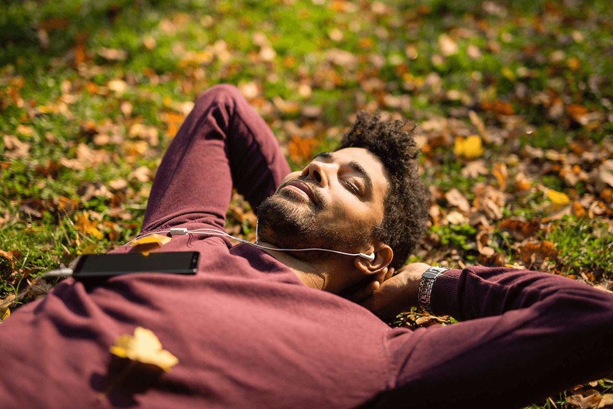 A man relaxes on the grass while listening to music.