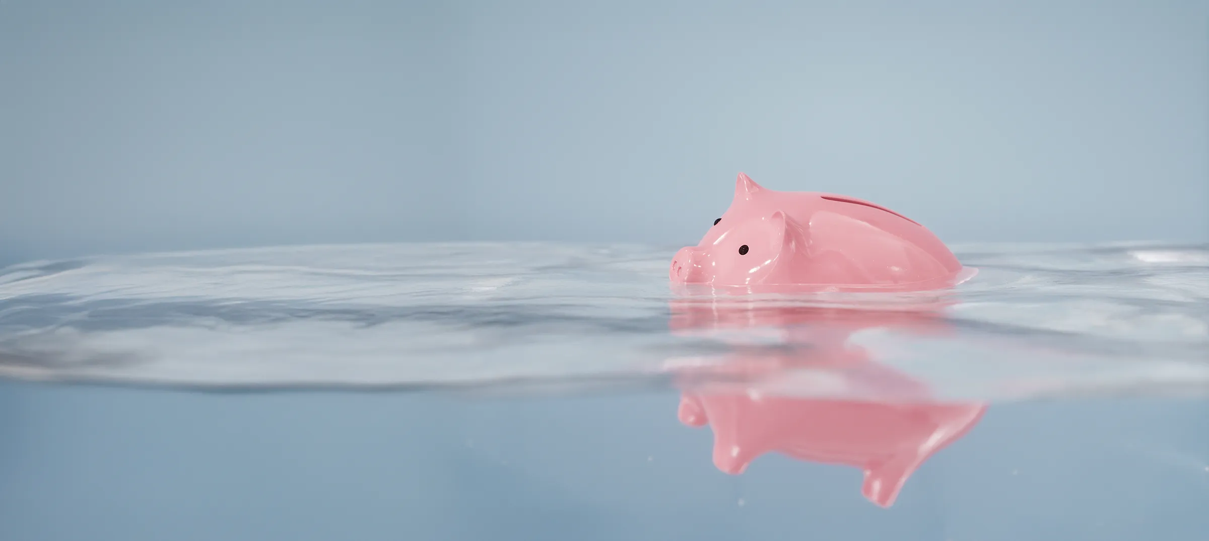 Une tirelire de couleur rose vif flotte dans l’eau, à moitié immergée.