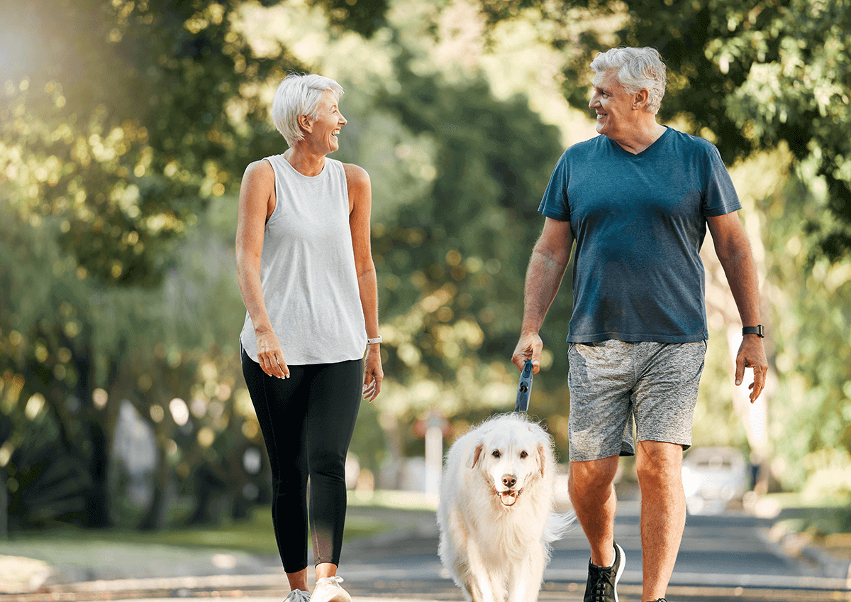 Deux aînés se sourient tout en se promenant tranquillement avec leur chien.