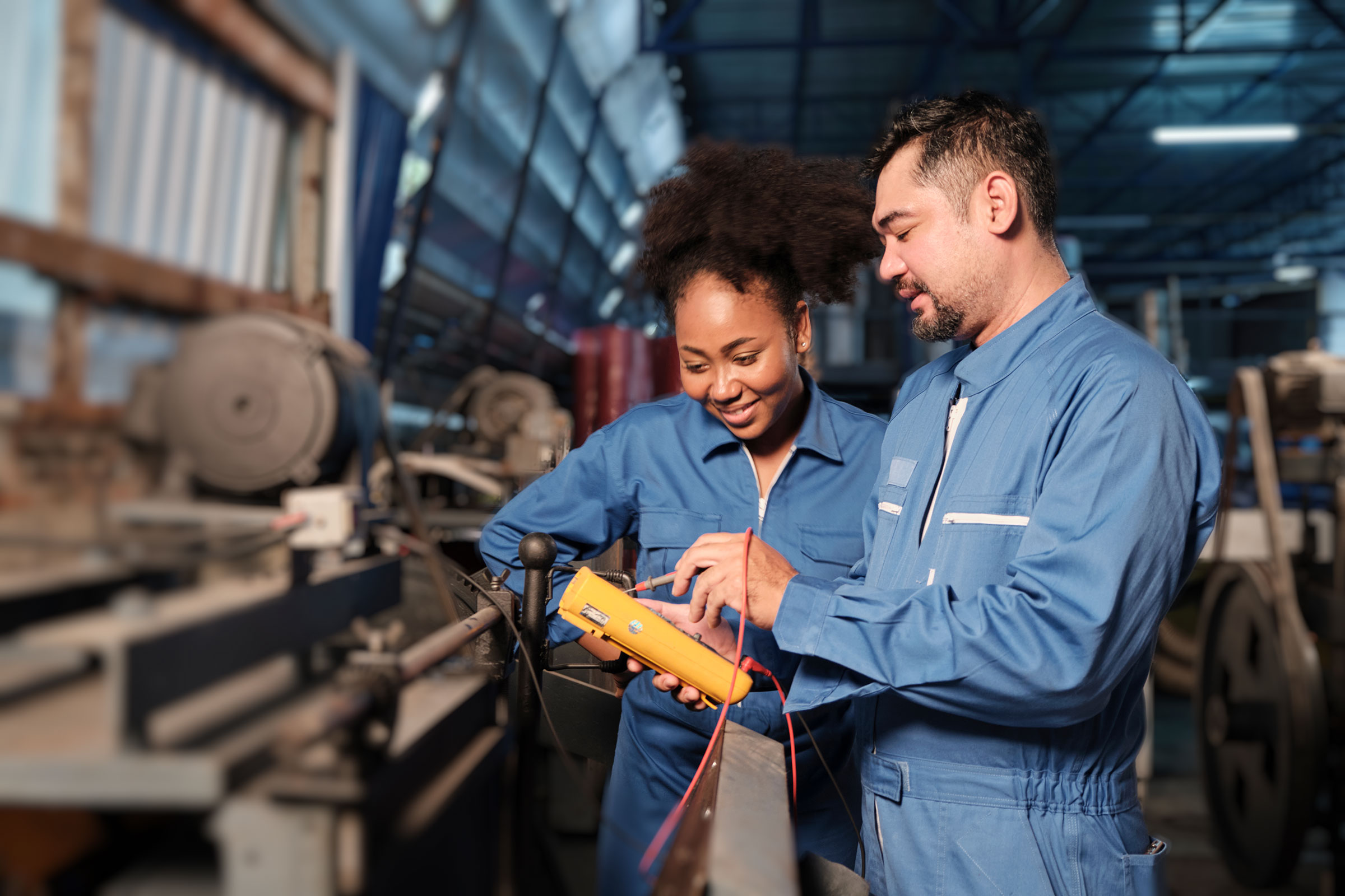 Un homme et une femme en habit de travail sont dans une usine et consultent un appareil électronique.