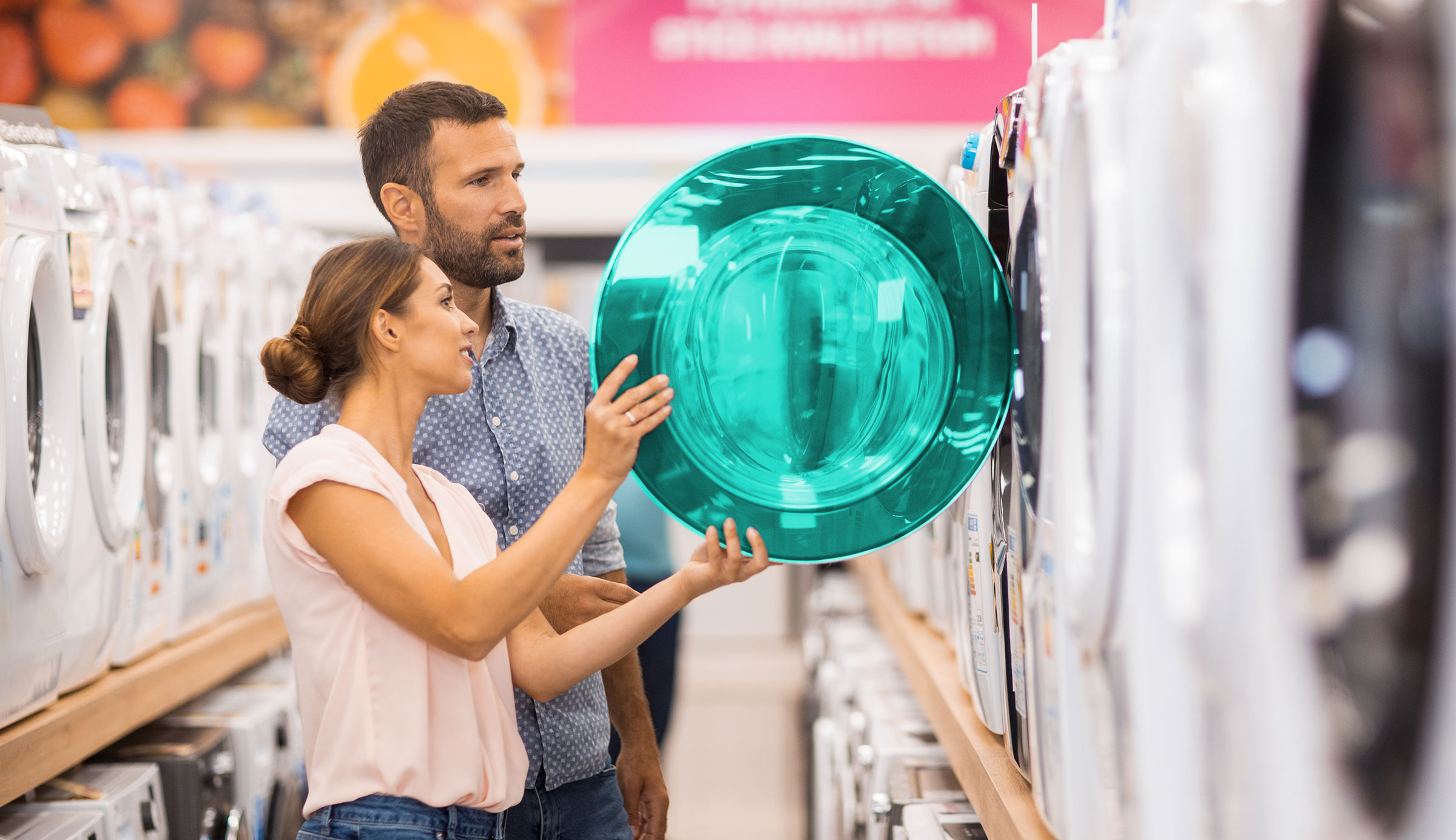 Un couple se tient dans un magasin, entouré d'appareils électroménagers. Ils regardent tous deux à l'intérieur d'une machine à laver ouverte.
