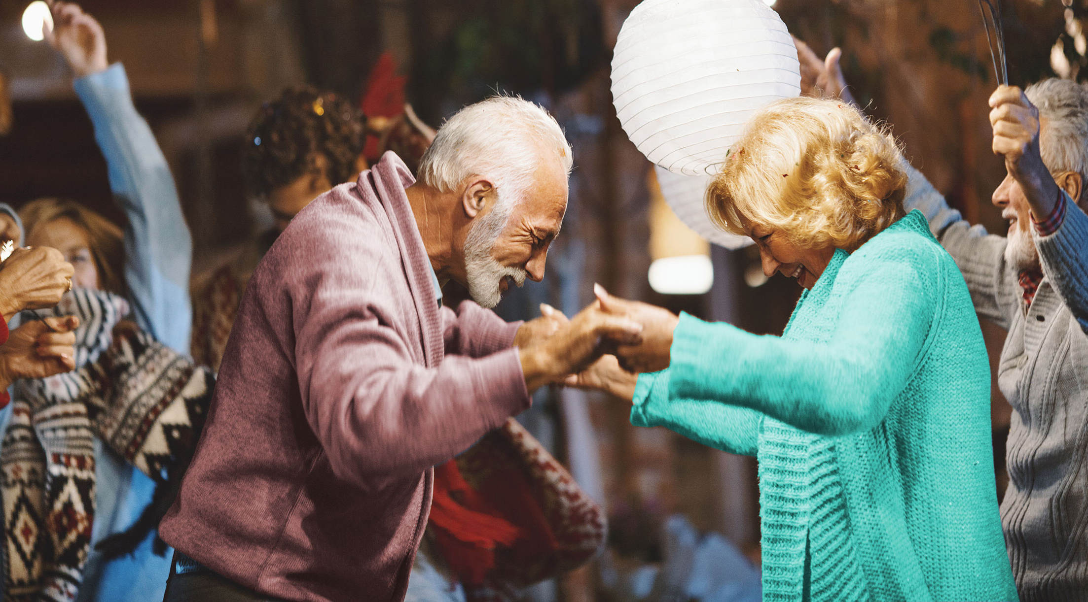 A senior couple dance and hold hands under the light of round lanterns.