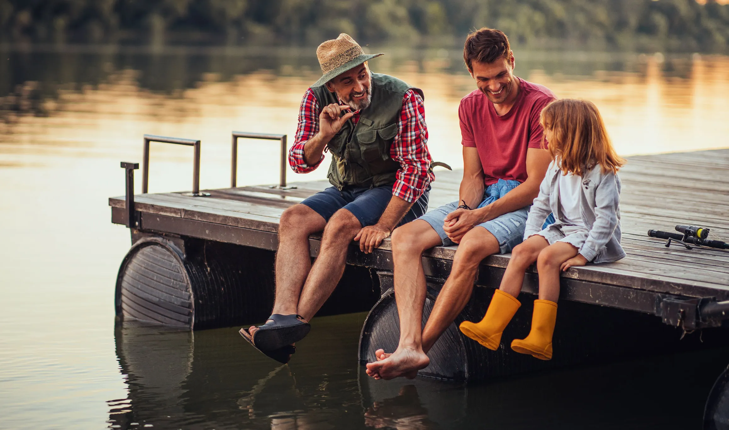 Un grand-père, un père et une fillette sont assis sur un quai, les pieds au-dessus de l’eau du lac.