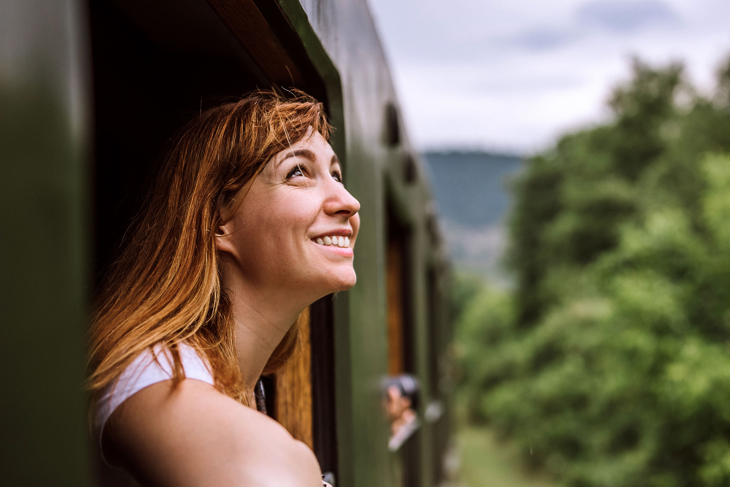 A woman smiling while looking out the window of a train.