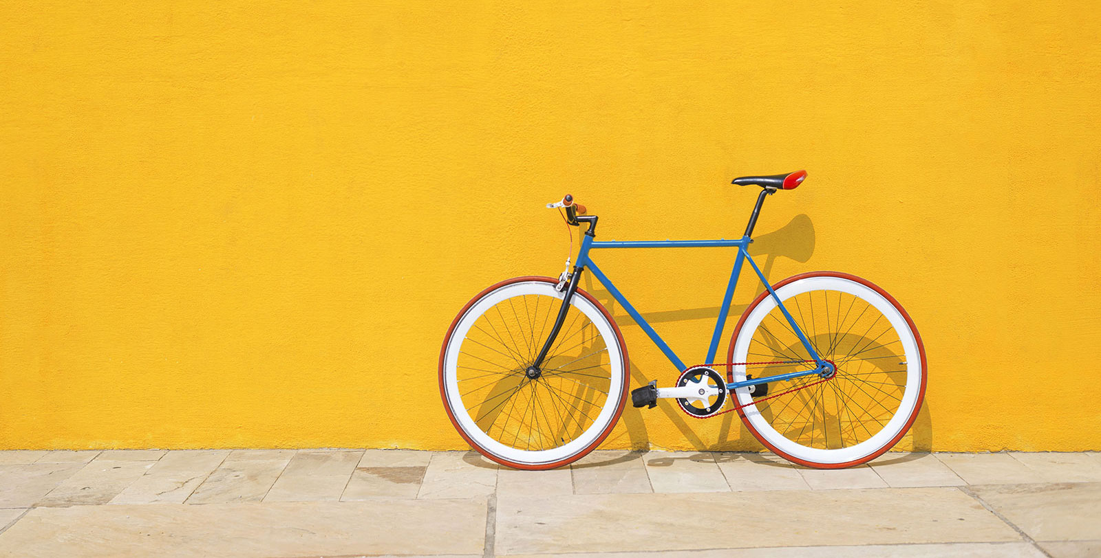 A blue, red and white bicycle leaning against yellow wall.