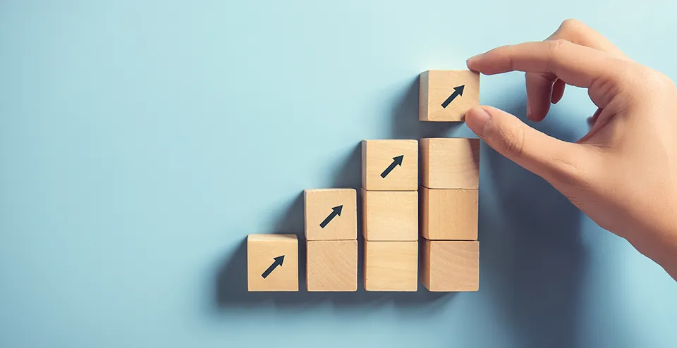 A hand arranges wooden blocks in rows. Together, they form a staircase-like chart with a few blocks with arrows pointing upward.