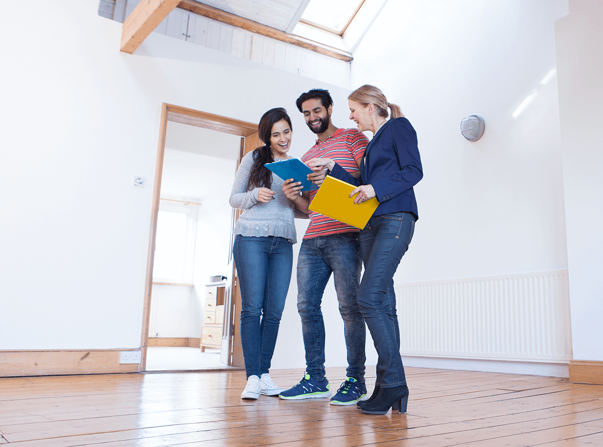 A young couple in their new home, accompanied by a home inspector, review a document.