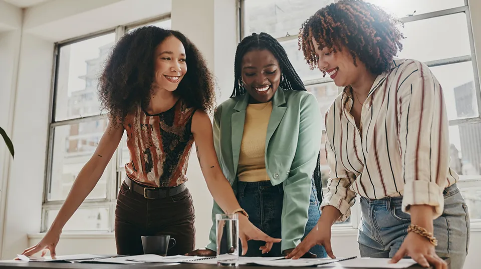 Three women smile and talk in a brightly lit office.