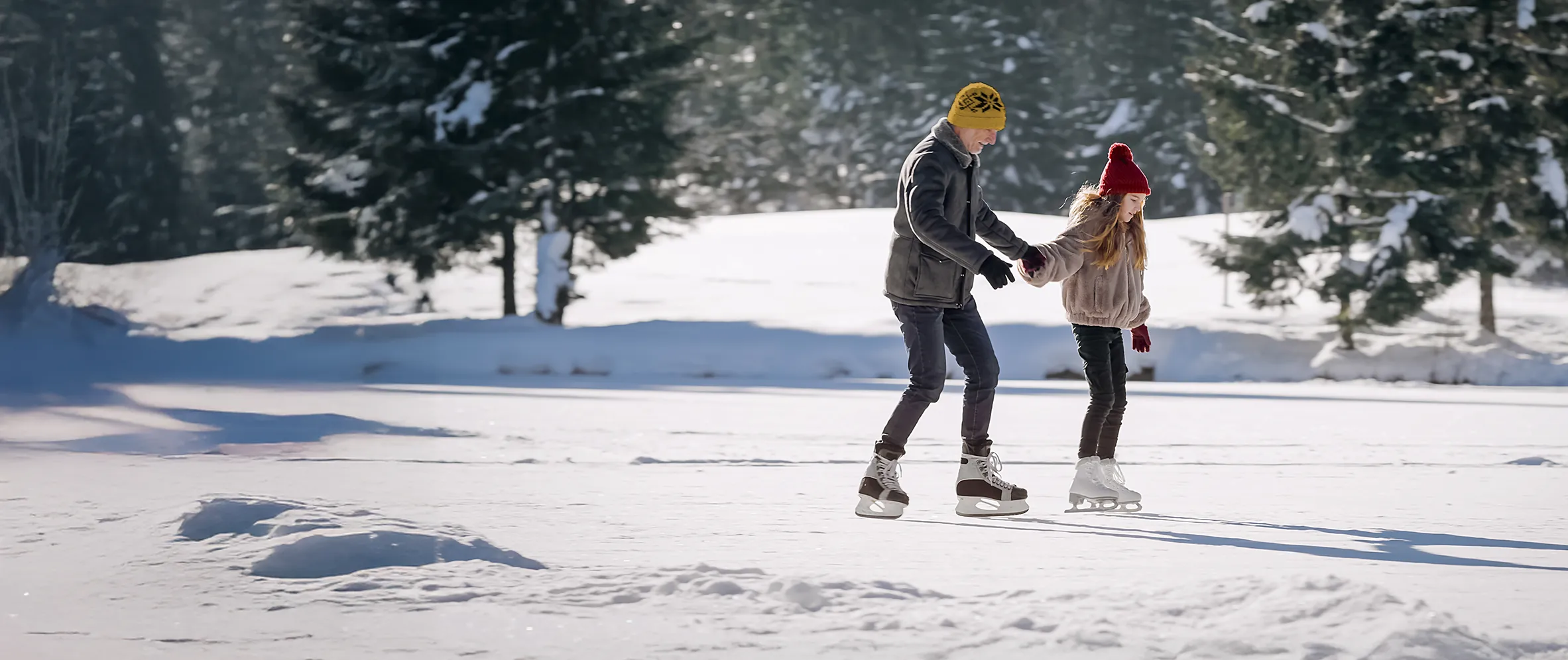 Un adulte et un enfant se tiennent par la main alors qu'ils patinent sur une patinoire extérieure.