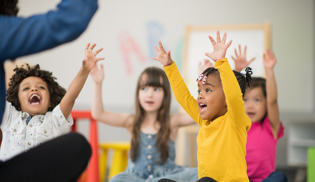 Young children in a daycare centre play gleefully with their hands in the air.