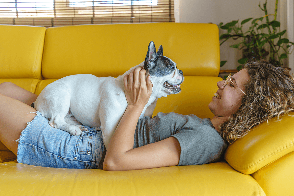 Une femme souriante allongée sur un canapé avec son chien.
