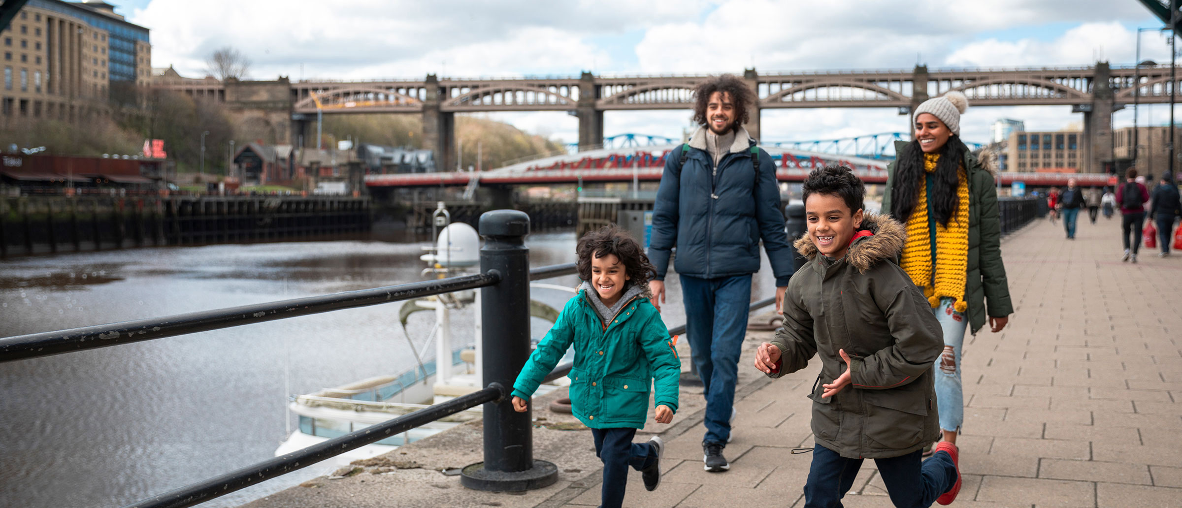 Children dressed for winter. run happily ahead of their parents as they walk along a pier.