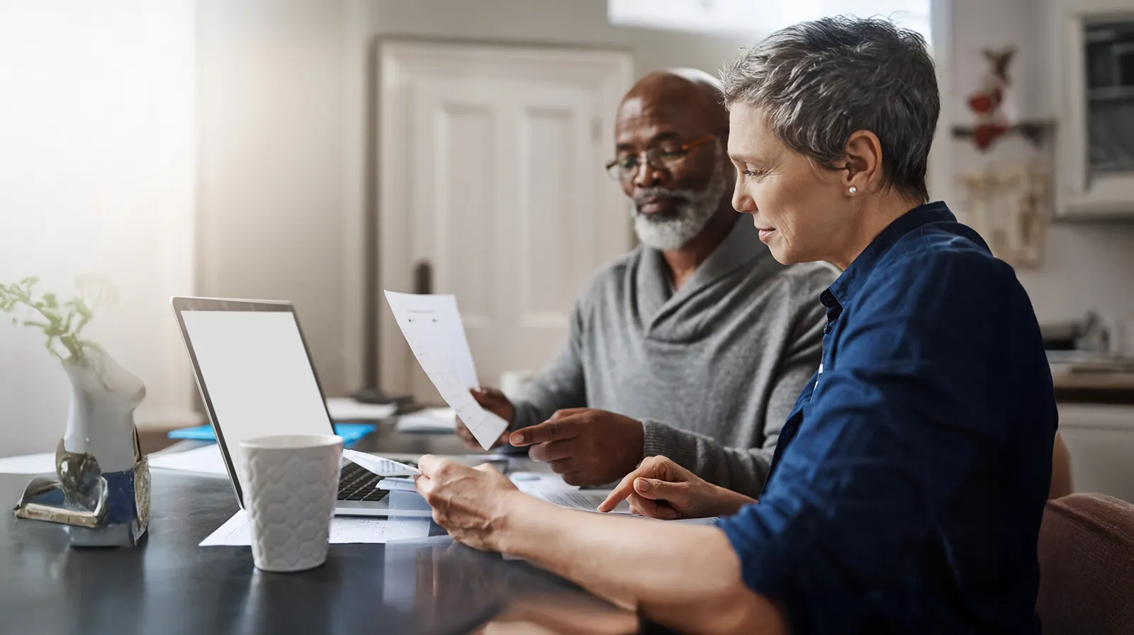 A couple reviews financial documents at home while working on a laptop.