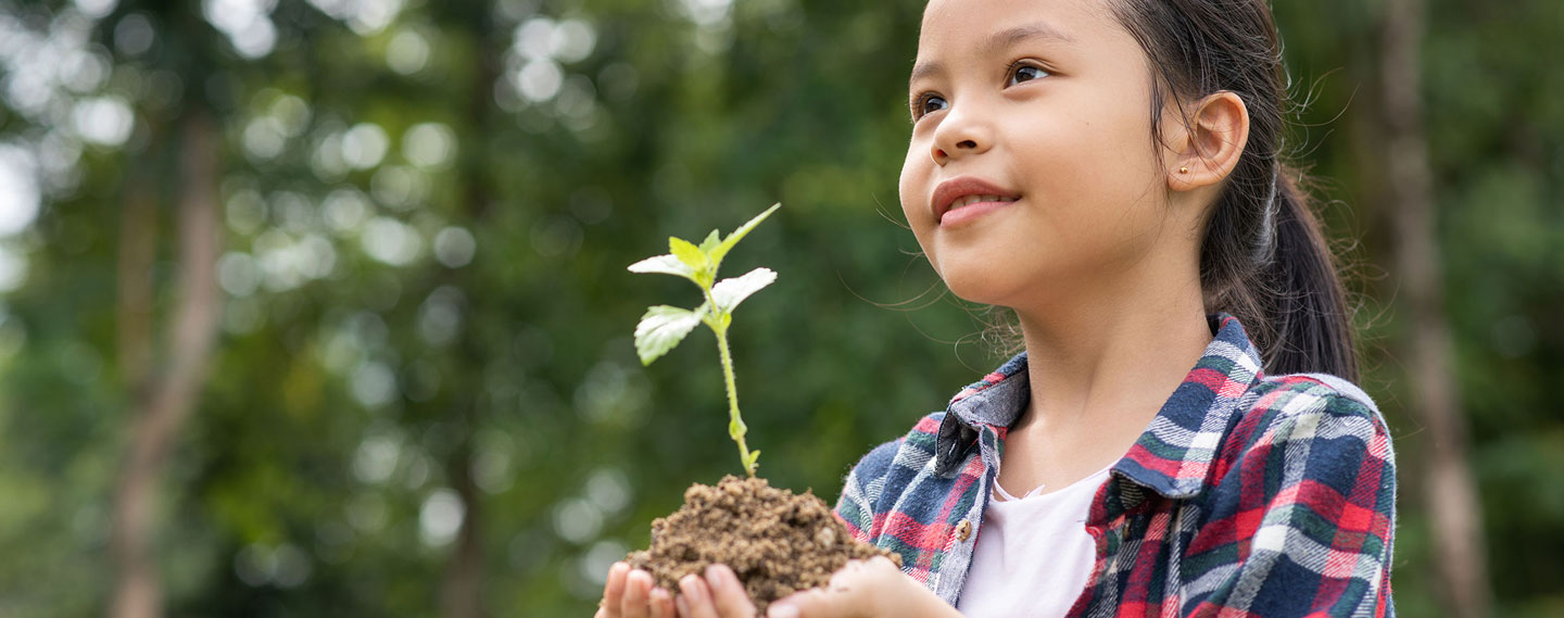 A girl holding a small plant in a mound of dirt.