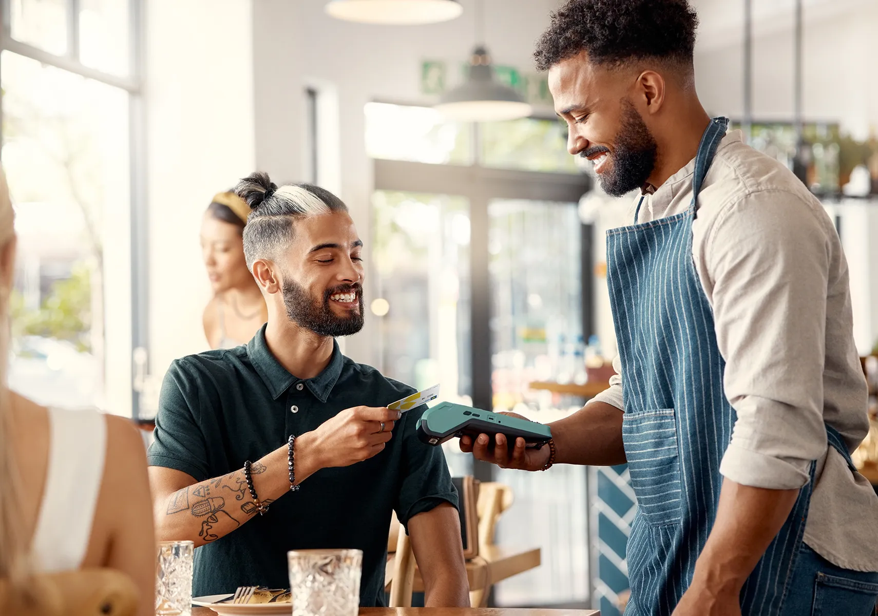 A man sitting in a restaurant pays for his meal by tapping his Laurentian Bank debit card on a wireless payment terminal held by the server.